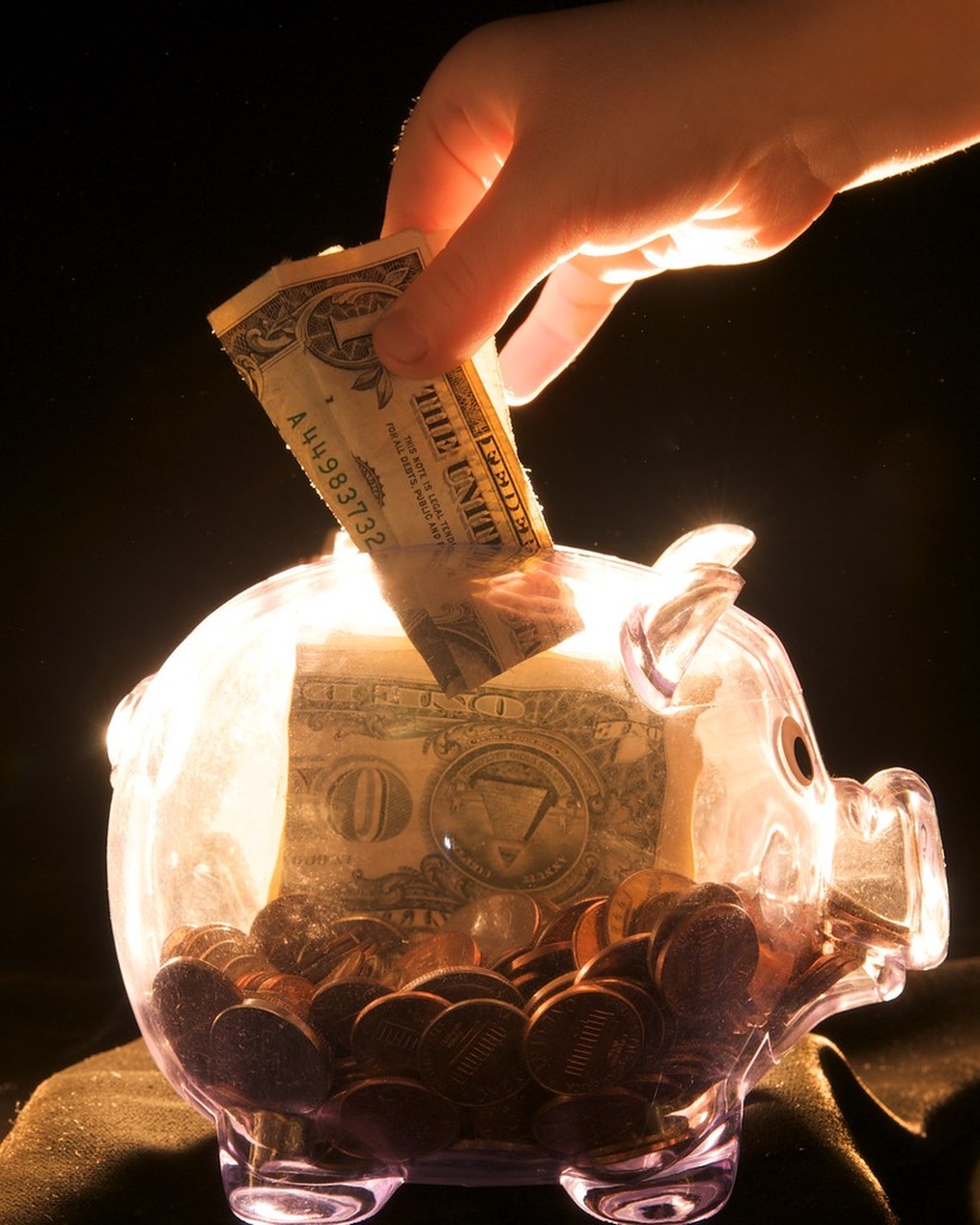 En hand lägger en sedel i en spargris, vilket symboliserar sparande som en del av finansiell planering.